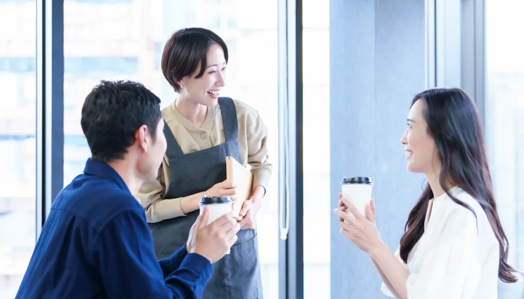 窓辺でコーヒーを片手に話す3人の社員